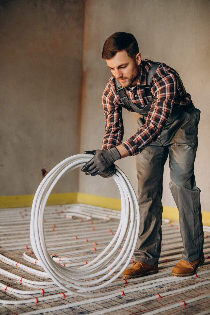 Trabajador instalando un sistema de calefacción por suelo radiante con tuberías PEX en una vivienda en construcción.